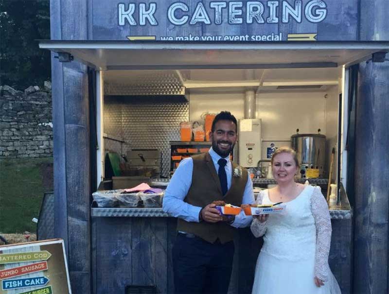 couple holding fish and chips next to catering van