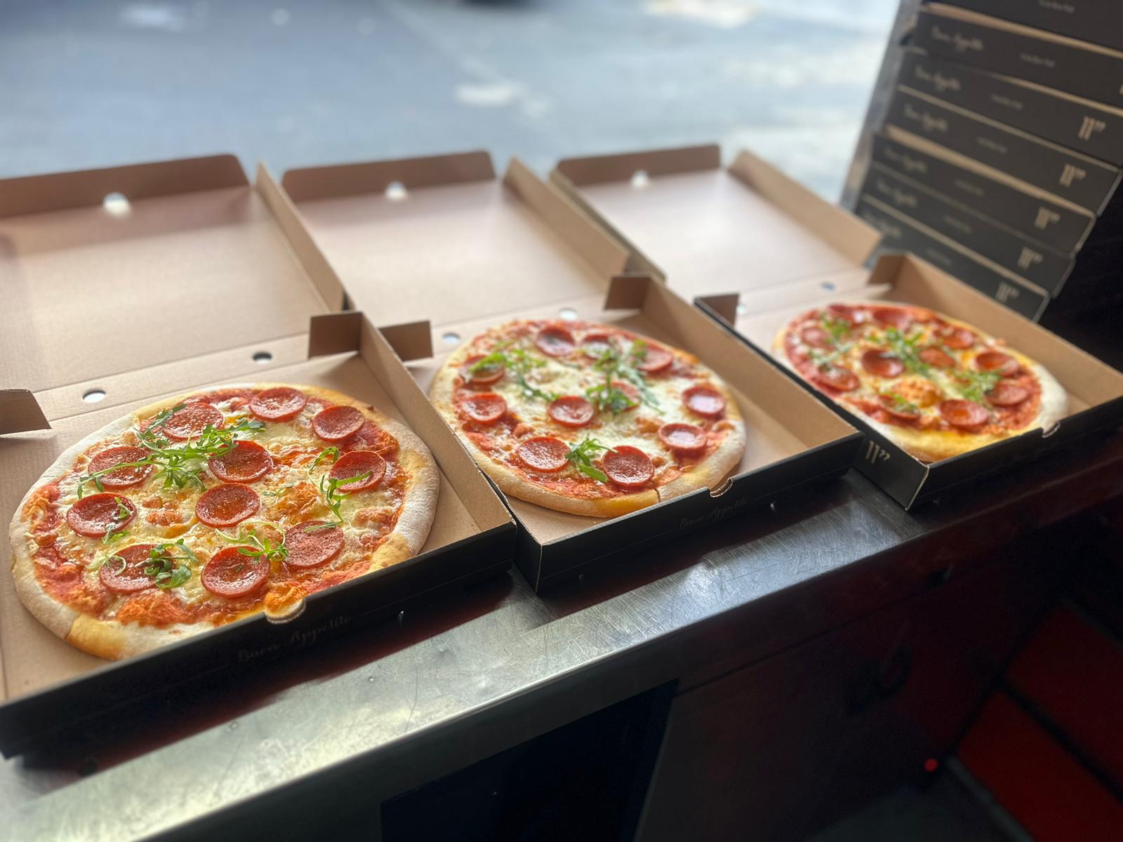 three pepperoni pizzas in pizza boxes on a kk catering van counter